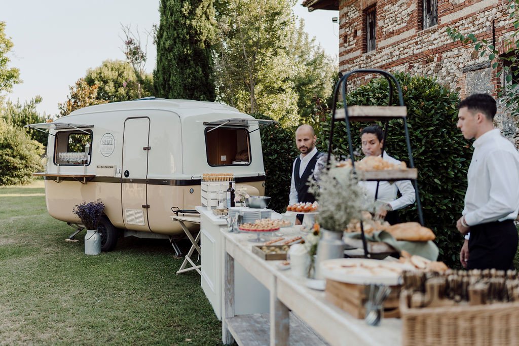 Food truck vintage beige con servizio catering all’aperto durante un matrimonio in giardino, con buffet rustico e personale in divisa