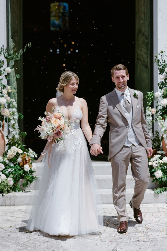 Bride and groom leaving the church after their wedding ceremony surrounded by flower petals