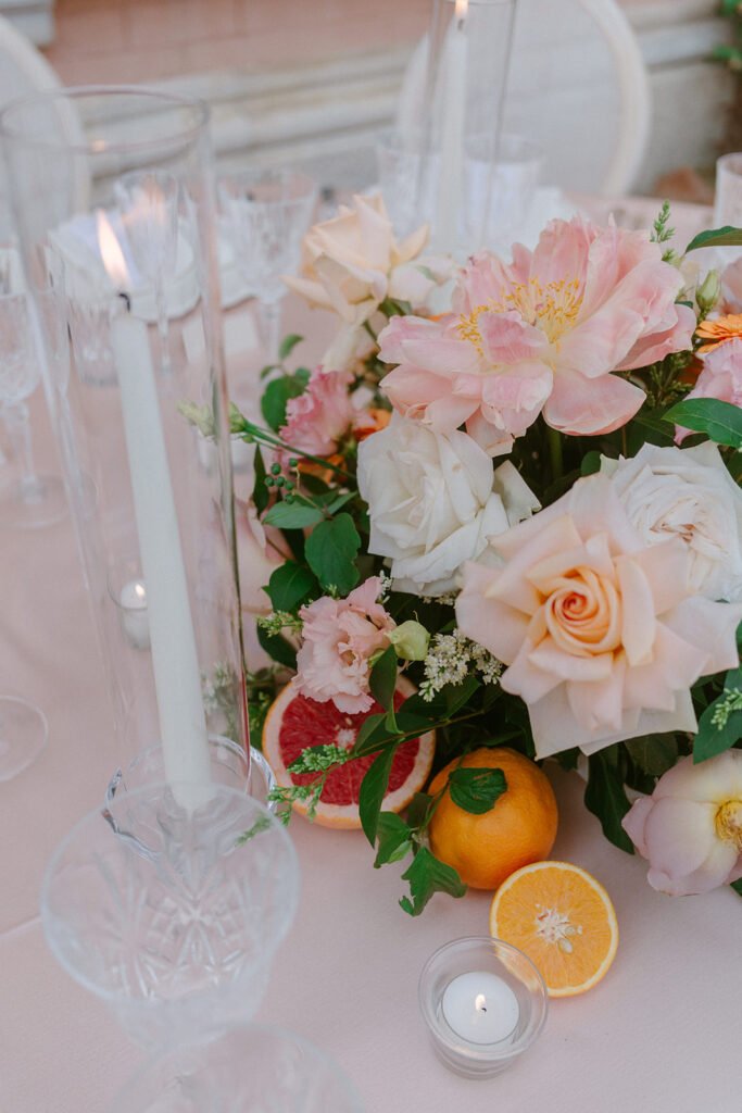 Floral wedding centerpiece with roses, peonies, citrus fruits and candles on the reception table