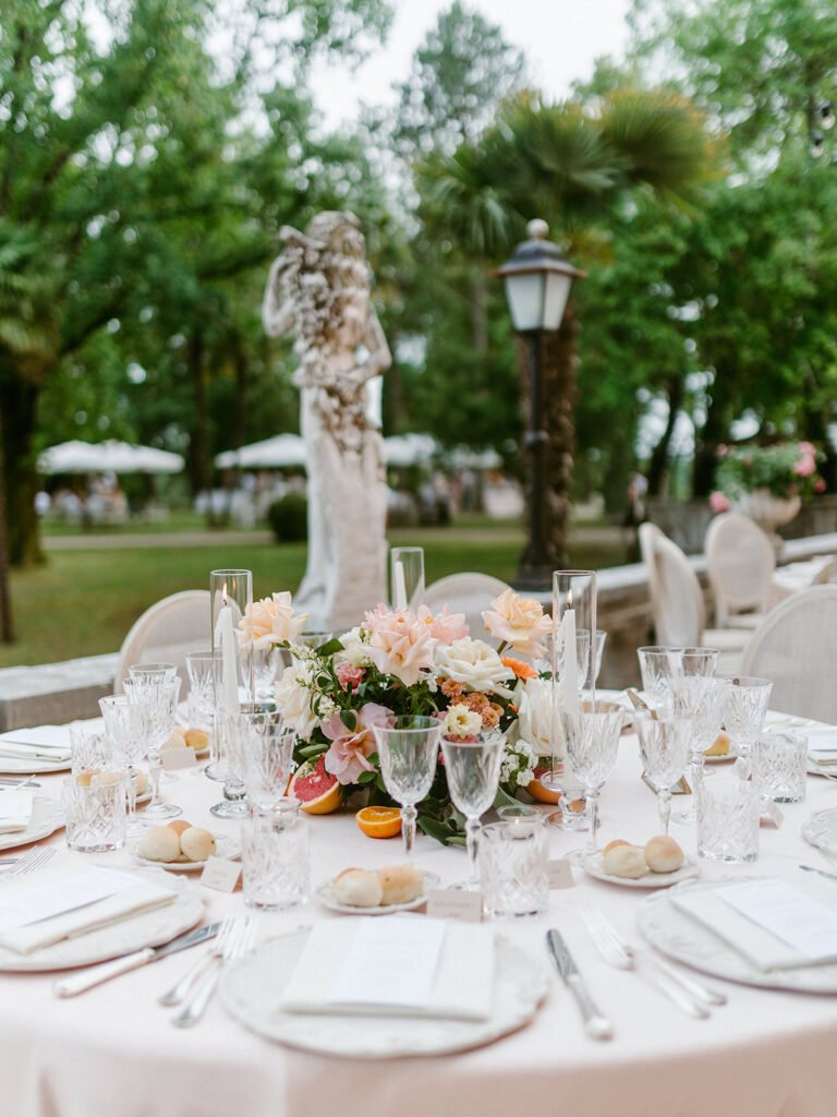 Floral wedding centerpiece with roses, peonies, citrus fruits and candles on the reception table