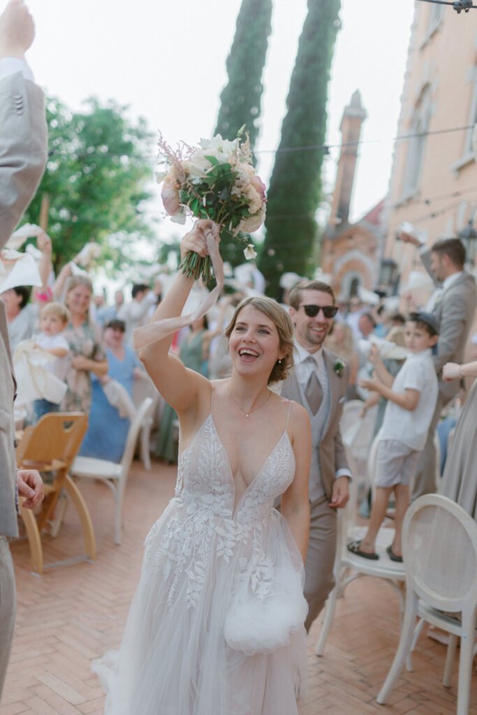 Bride celebrating with her bouquet after the wedding ceremony surrounded by guests